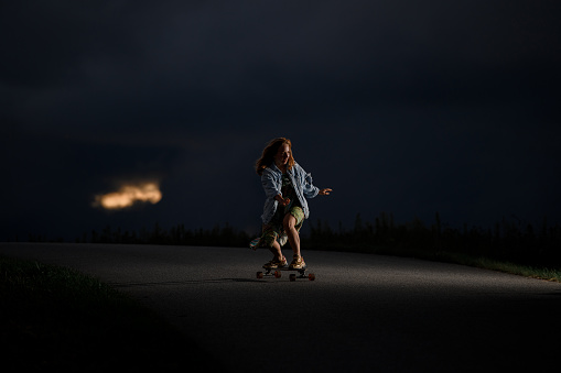 Young girl rides along the road standing on a longboard a background of a sky with clouds through