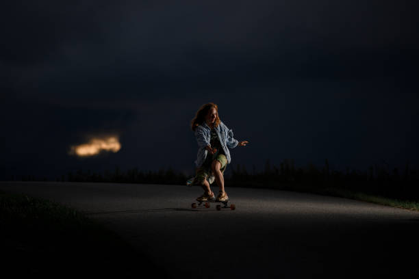 młoda dziewczyna jedzie wzdłuż drogi stojąc na longboardzie z nogami ugiętymi w kolanach - knees bent zdjęcia i obrazy z banku zdjęć