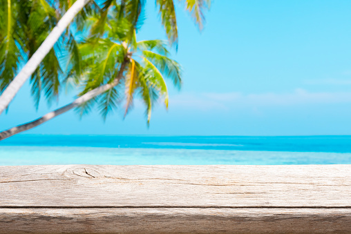 Aged wooden table top on blurred tropical sea and coconut palm trees background