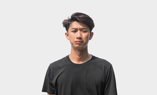 A young Asian man in his 20s wearing black t-shirt is depressed and worried in distress standing on a gray background. Crying in anger and fear. Sad expression concept