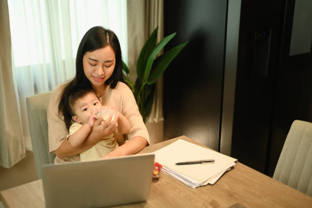 istock Caring mother feeding milk from bottle to her baby while working remotely at home 2080309858