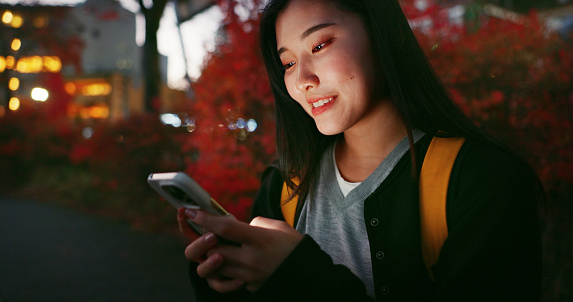 Happy asian woman, phone and night at city for social media, communication or outdoor networking. Female person smile on mobile smartphone in late evening for online chatting in urban town of Japan