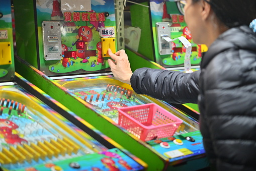 Taiwan - Feb 28, 2024: At a pinball stall in Ningxia Night Market in Taiwan, a close-up of a customer playing a pinball machine, the player is about to insert a coin into the machine.