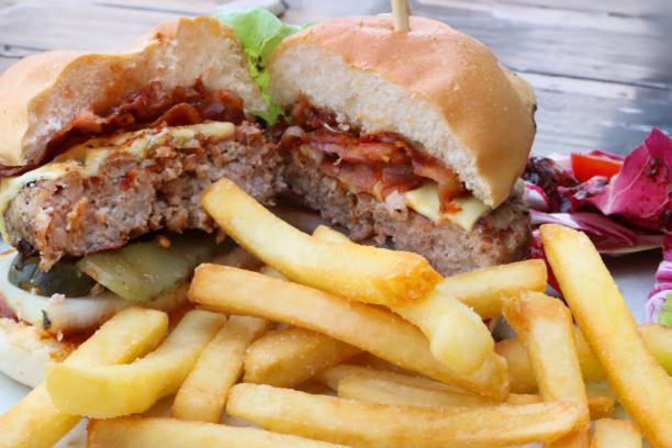 Stock photo showing close-up view of a meal of bacon cheeseburger in a white bread bun served with crunchy French fry chips.
