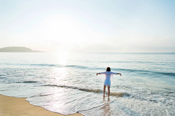 istock Young woman standing on beach with arms outstretched 2080338856