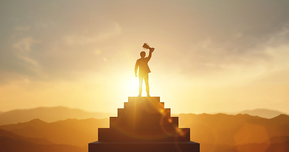 Silhouette of businessman holding a trophy on top staircase with light sunset. concept of a successful business or determination to lead the organization to success.