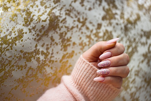 An image featuring a woman's hand with stunning pink gel nails, meticulously painted and adorned with stylish multicolored glitter. The hand is well-maintained and nourished.