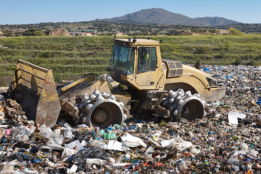 Heavy machinery shredding garbage in an open air landfill. Waste