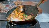 Preparing Stir-Fried prawns with snow peas and red capsicum in a wok