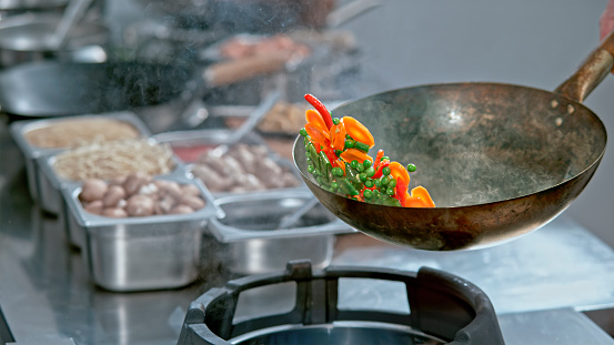 Close-up of carrots, chilli and peas being tossed in the wok while being stir fried at restaurant kitchen.