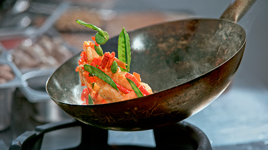 Close-up of preparing stir-fried prawns with snow peas and red capsicum in a wok.
