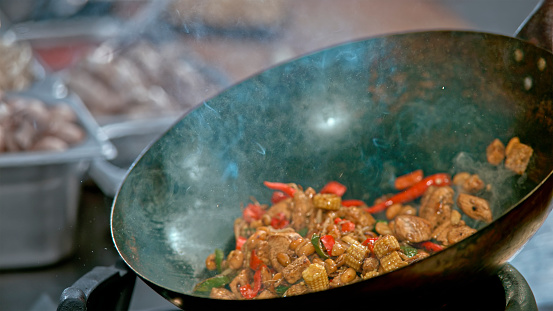 Close-up of a stir fry chicken and vegetables in a wok on a stove.