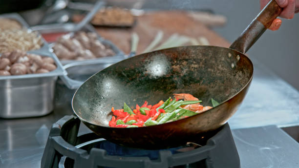 Close up of Stir-Fried prawns with snow peas and red capsicum in a wok at restaurant kitchen.