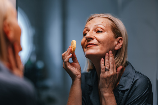 Close up shot of a beautiful senior woman applying make up with a sponge as a part of her morning beauty routine.