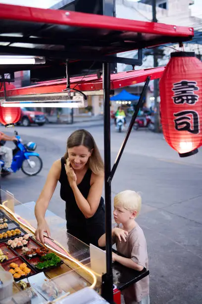 A mother shops with her 6 year old son at a street market in Thailand during their vacation in Asia