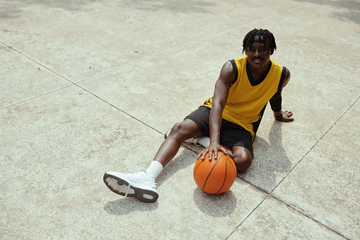 Black streetball player resting on ground after game and smiling at camera