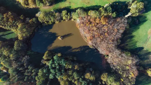 Drone photo over a pond and forest with autumn colors in the Dordogne, near the Château de Biron.