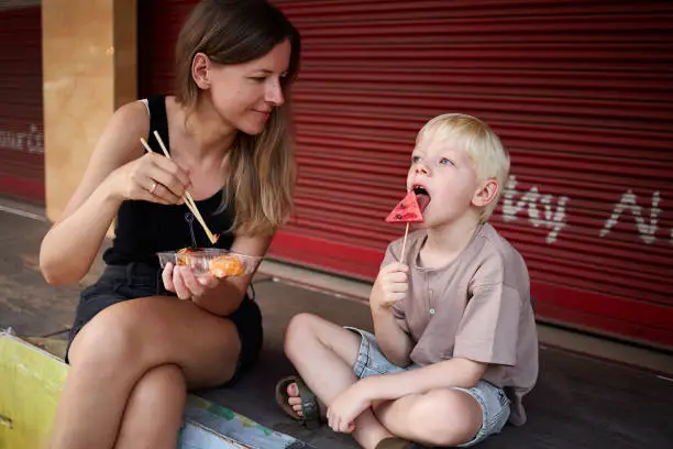 A mother takes a break to eat with her 6 year old son at a street market in Thailand during their vacation in Asia
