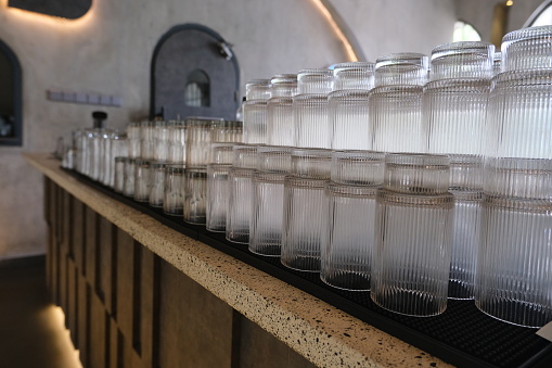 Row of clean ribbed glass tumblers lined up on a modern bar counter with a moody ambiance.