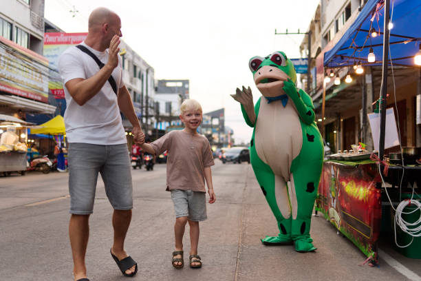A father walks with his 6 year old son through a night market in Thailand during their vacation in Asia