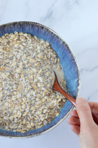 Female hand holding spoon and eating oatmeal breakfast bowl with chia seeds and plant-based milk. Top view. Close-up. Organic vegan food, healthy dieting concept.