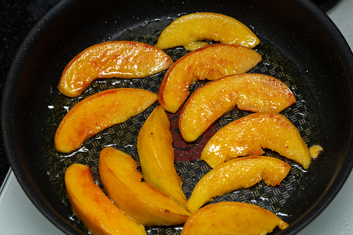 Frying peach slices in butter in a frying pan