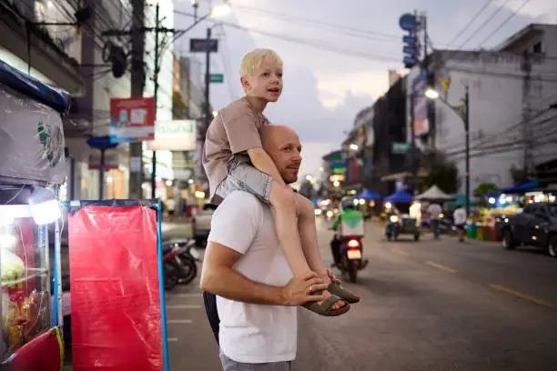 A father walks with his 6 year old son through a night market in Thailand during their vacation in Asia