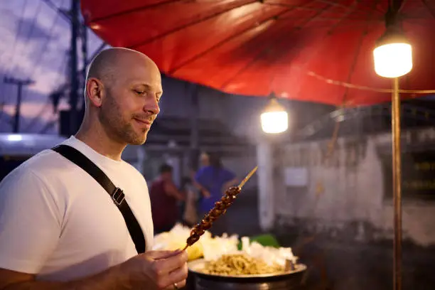 A man tastes food at a night market in Thailand during his vacation in Asia