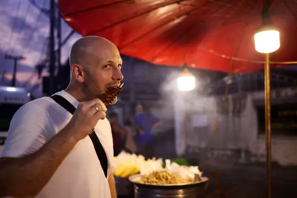 A man tastes food at a night market in Thailand during his vacation in Asia
