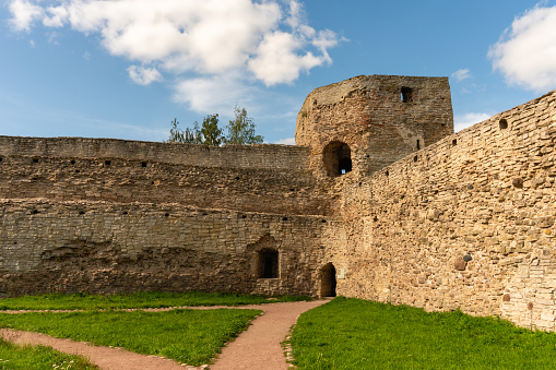 Walls of an old Russian fortress made of local stone with traces of time and destruction, watchtowers with embrasures, powerful defensive structures, fortification architecture, history and culture, city landmark, autumn view.