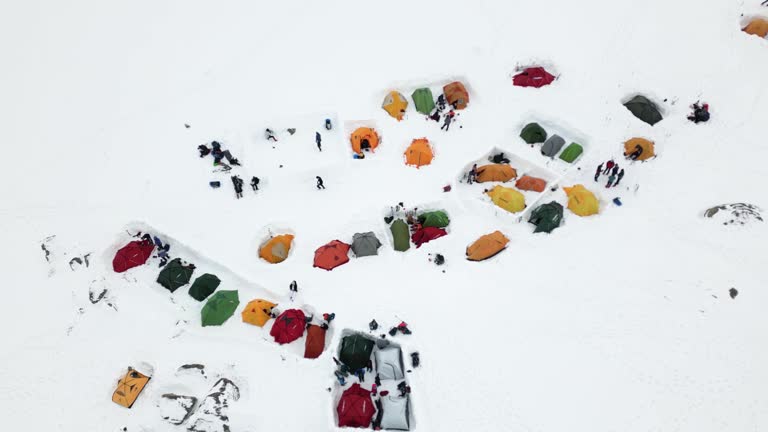 Aerial view of a camping site filled with multicolored camping tents in the middle of snow snow-covered mountain.