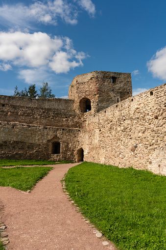 Walls of an old Russian fortress made of local stone with traces of time and destruction, watchtowers with embrasures, powerful defensive structures, fortification architecture, history and culture, city landmark, autumn view.