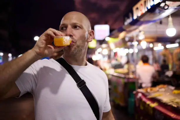 A man tastes juice at a night market in Thailand during his vacation in Asia