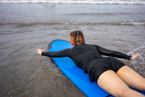 Rear view of an Asian female surfer paddling into the ocean