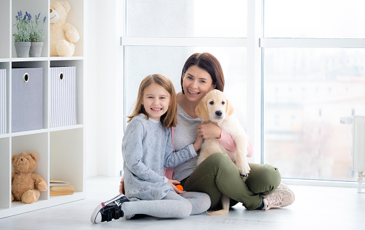 Cheerful woman and girl holding retrtiever dog sitting at home
