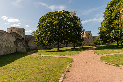 Walls of an old Russian fortress made of local stone with traces of time and destruction, watchtowers with embrasures, powerful defensive structures, fortification architecture, history and culture, city landmark, green trees and lawns, autumn view.