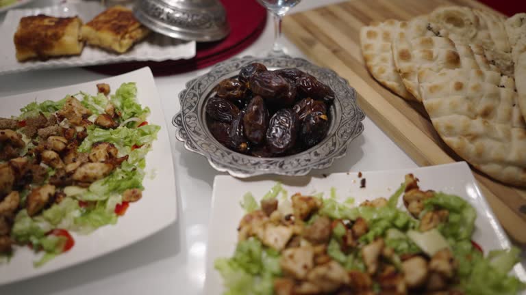 Ramadan Evening Meal Zoom In Shot of the Dates Served in a Vintage metal bowl by chicken salad, flatbread, and a glass of water served on a table for Muslims to break the fast