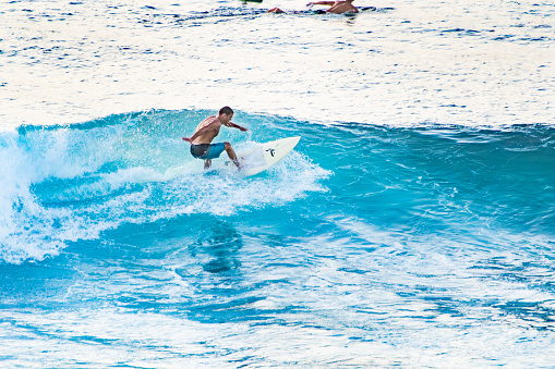 Bali, Uluwatu - A surfer, balanced on a surfboard, rides a turquoise wave. The clear blue ocean on the background.