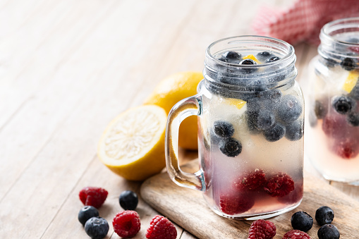 Fresh berry drink with blueberries and raspberries and lemon on wooden table.
