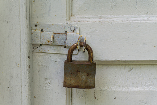 An old, roughly painted white door with a deadbolt and a rusty padlock. Paint smudges and wood texture are visible.
