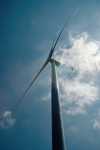 Slim wind turbine with rotor blades at top illuminated by sunlight. Windmill producing renewable form of clean energy from wind