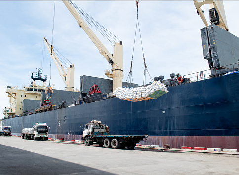 Ship loading cargo at port terminal, ship crane lift sling of sugar bags onto a vessel. Transportation and shipping of agricultural products for export.
