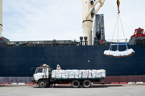 Loading bag cargo at seaport, ship crane lifting sugar bag onto ship hole.