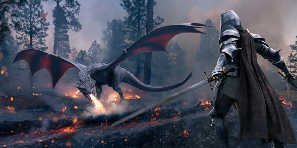 A medieval knight dressed in full period armour and cape standing with two swords drawn about to do battle with a dragon in a smoke filled forest with burning trees and charred wood on the ground.