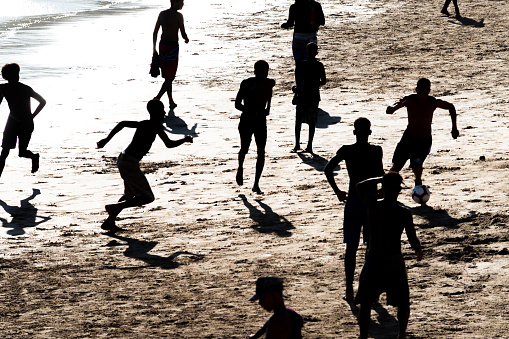 Salvador, Bahia, Brazil - February 14, 2019: Young people, in silhouette, are seen playing beach soccer on Ondina beach during sunset in Salvador, Bahia.