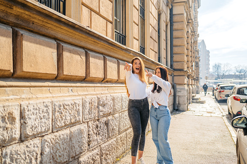 Two beautiful female friends pointing and laughing in the city.