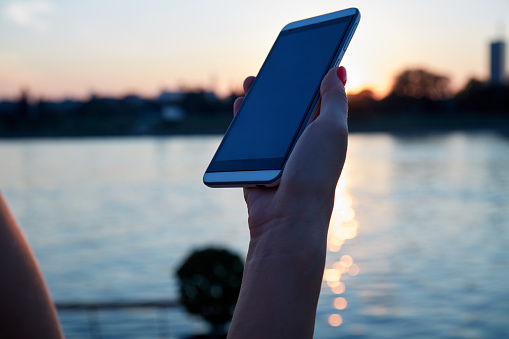 Woman holding cellphone outdoors in sunset time.