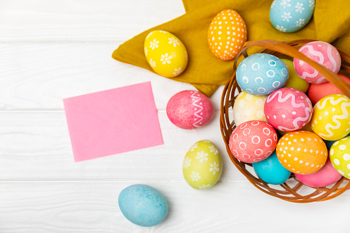 Easter basket filled with colorful eggs and a bouquet of tulips on a textured wooden table. Easter celebration concept. Colorful easter handmade decorated Easter eggs. Place for text. Copy space