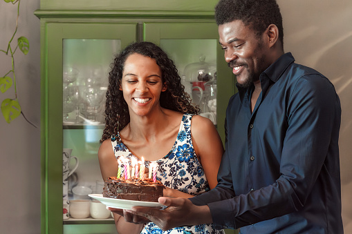 young man holding birthday cake with burning candles for young woman