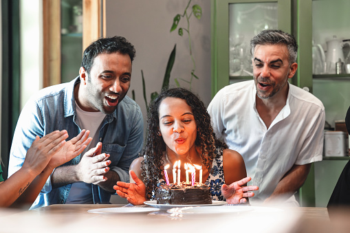 young woman blowing out candles on birthday cake surrounded by friends